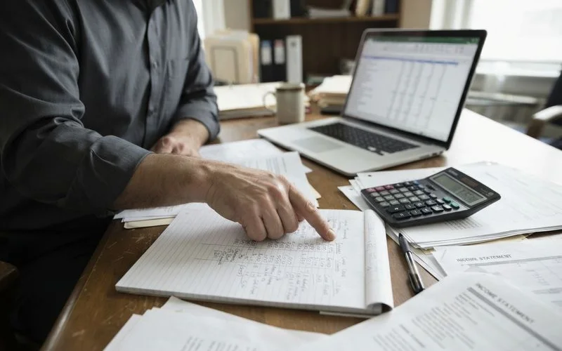 A calculator, pay stubs, and a notepad with monthly budget figures laid out on a table