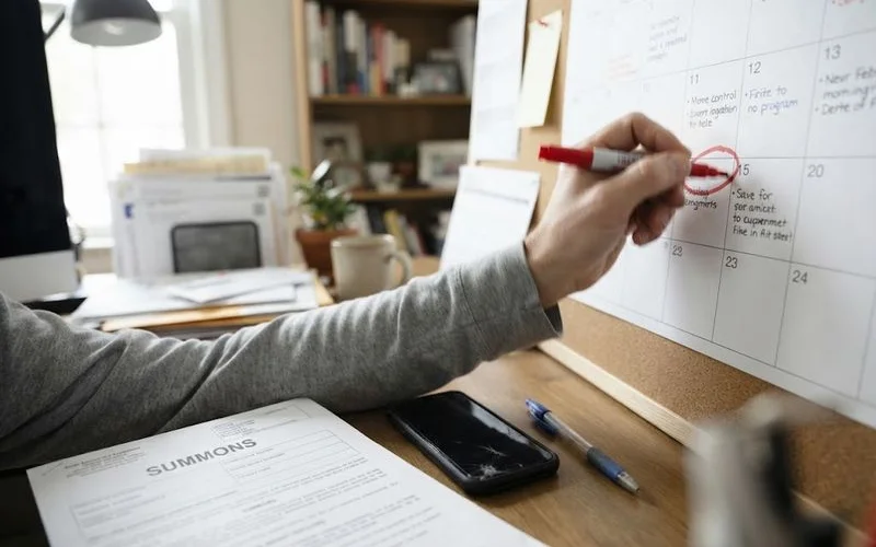 A person circling a court deadline date on a wall calendar next to a folder of foreclosure paperwork